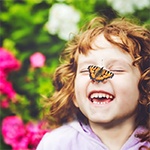 child laughing with a butterfly on their nose