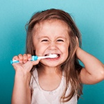 A little girl with messy hair using a child’s toothbrush to clean her teeth in the morning