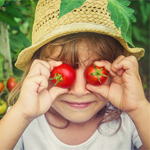 child holding ripened tomatoes up to their eyes to be goofy